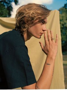 a young man is holding his hand up to his face while wearing a black shirt