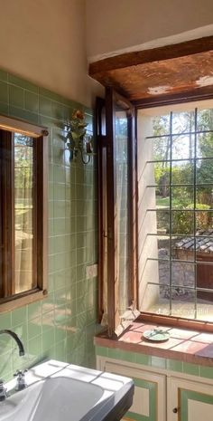 a bathroom with green tile and wooden trimmings on the window sill, along with a white sink