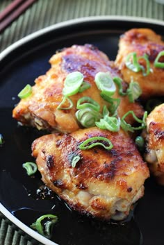 four pieces of chicken on a black plate with green garnishes and chopsticks