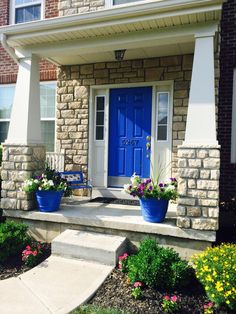 a blue front door with two planters on the steps next to it and flowers