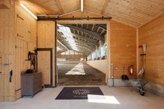 the inside of a barn with an open door and horse stalls on either side of it