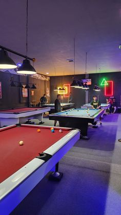 a group of people playing pool in a room with neon signs on the walls and tables