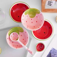 three watermelon bowls and two spoons on a white table with fruit plates