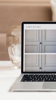 an open laptop computer sitting on top of a white table next to a glass vase