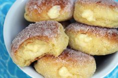 powdered sugar covered doughnuts in a bowl on a blue tablecloth with water