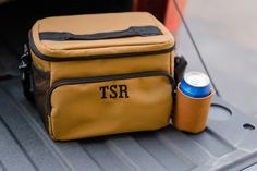 a cooler bag sitting in the trunk of a car with its lid open and two cans next to it