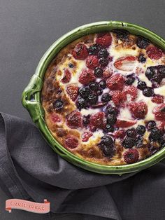 a small pizza with berries and cheese in a green dish on a gray tablecloth