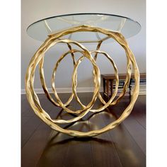 a glass table with gold colored metal rings on it's top and wooden flooring