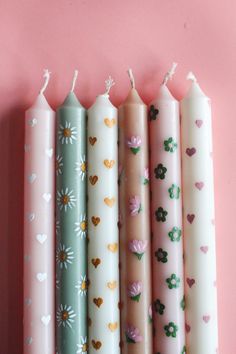 four candles are lined up against a pink wall with hearts and flowers painted on them