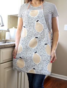 a woman standing in front of a kitchen counter wearing an apron with apples on it