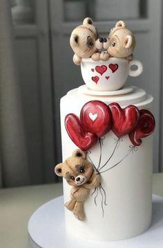 two teddy bears sitting on top of a cake with red balloons and heart shaped balloons