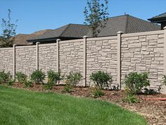 a brick wall in front of a house with green grass and flowers next to it