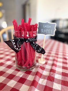 some red and white straws are in a glass on a checkered table cloth