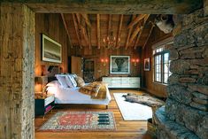 a bedroom with wood paneling, stone walls and a bed in the center surrounded by rugs