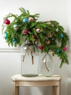 two glass vases with christmas ornaments on top of a table next to a wall