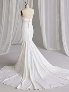 the back of a wedding dress on a mannequin stand in front of white drapes