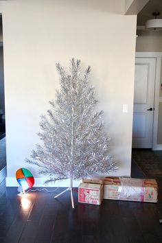 a silver christmas tree sitting on top of a hard wood floor next to two wrapped presents