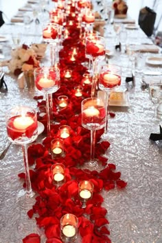 a long table with candles and red rose petals on the runner, along with wine glasses