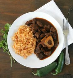 a white plate topped with meat and rice next to green peppers on top of a wooden table