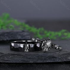 two wedding rings sitting next to each other on top of a black stone slab with greenery in the background