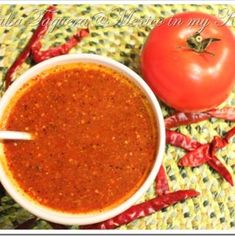 a bowl of chili sauce next to a tomato