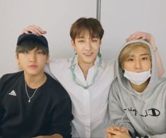 three young men sitting next to each other in front of a white wall wearing masks