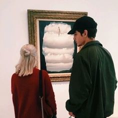 a man and woman standing in front of a painting on the wall looking at each other