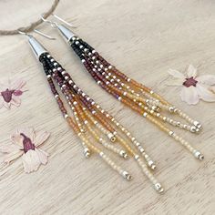 three pairs of beaded earrings on top of a wooden table next to pink flowers