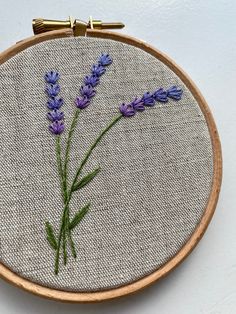 a close up of a embroidery on a wooden hoop with purple flowers in the middle