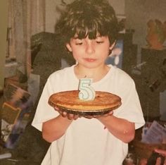 a young boy holding a cake with the number five on it in front of him