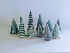 small ceramic trees are lined up in a row on a white surface, one is green and the other is blue