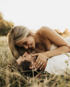 a beautiful blonde woman laying on top of a man's chest in the grass