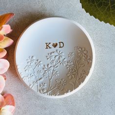 a white bowl with the word kod written on it next to some pink flowers