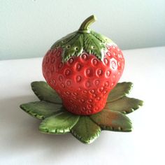 a ceramic strawberry sitting on top of a leaf