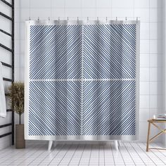 a bathroom with a shower curtain that has diagonal stripes on it, next to a stool and towel rack