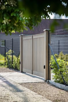 a wooden gate in front of a fenced area with plants and bushes around it