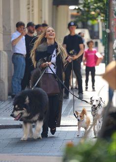 a woman walking two dogs on a leash down the street while others walk behind her