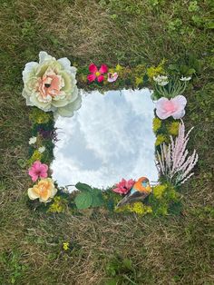 a mirror sitting on top of a grass covered field with flowers and birds in it