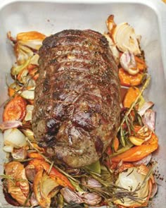 a large piece of meat sitting on top of a pan filled with vegetables and herbs