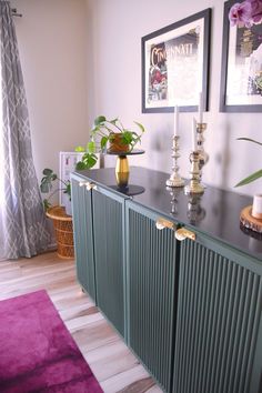 a sideboard with candles and flowers on it in front of two pictures hanging on the wall