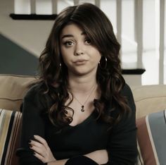 a woman sitting on top of a couch with her arms crossed and looking at the camera