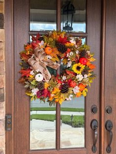 a wreath on the front door with autumn leaves and pinecones hanging from it