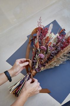 someone is arranging dried flowers on top of a blue mat with brown ribbon around it