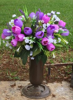 a vase filled with purple and white flowers on top of a stone slab in the grass