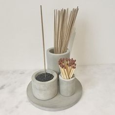 two cement cups with sticks in them on a marble countertop next to a cup filled with incenses