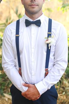 a man in a white shirt and blue suspenders is wearing a black bow tie