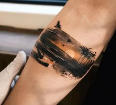 a person with a tattoo on their arm that has a sunset and palm trees in the background