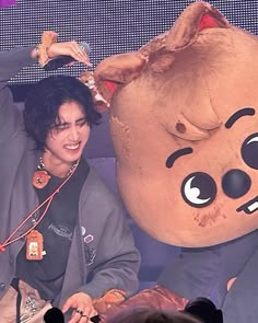 a man sitting next to a giant stuffed animal on top of a stage in front of a crowd