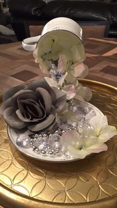 a white and gray flower sitting on top of a gold tray next to a cup