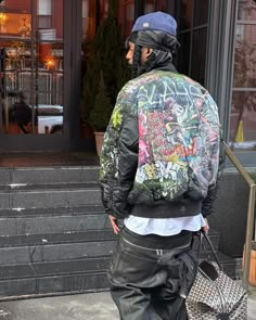 a man walking down the street carrying a bag and wearing a jacket with graffiti on it